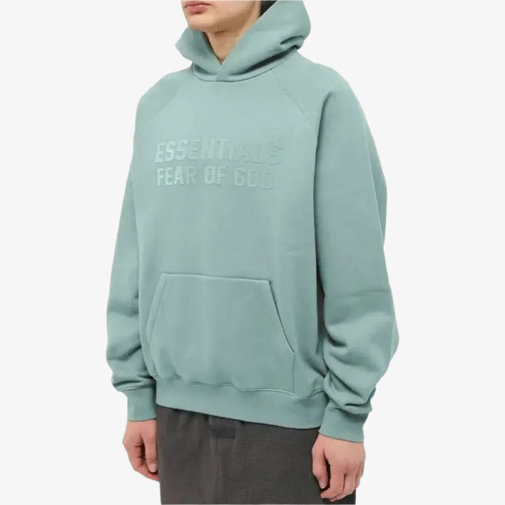 Fear of God Essentials hoodie in Sycamore color, featuring a relaxed fit and logo design, displayed on a hanger.
