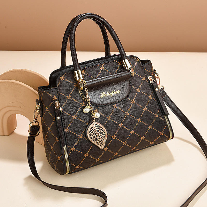 Black handbag with gold accents and a decorative charm on a beige background
