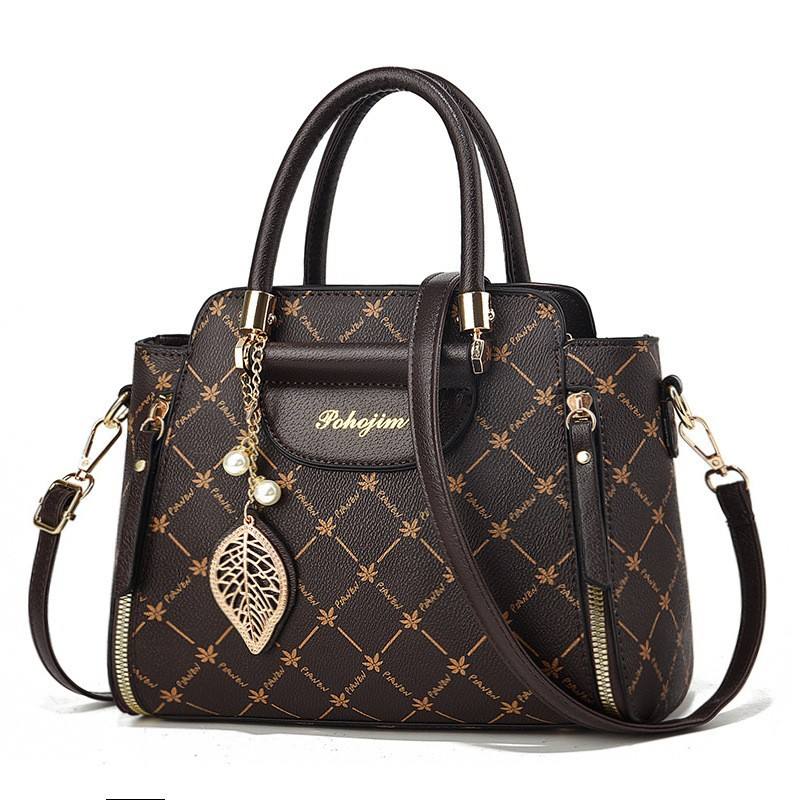 Black handbag with gold accents and a decorative leaf charm on a white background