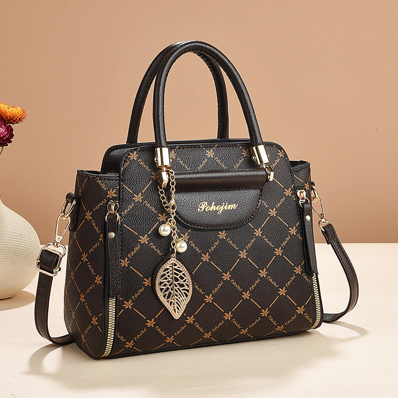 Black handbag with gold accents and a decorative pendant on a beige background
