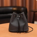 Black leather drawstring bag on a wooden surface with a blurred background