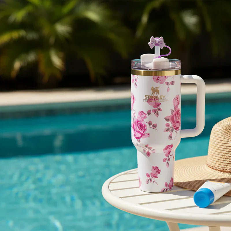 Floral-patterned tumbler with straw on a table by a pool