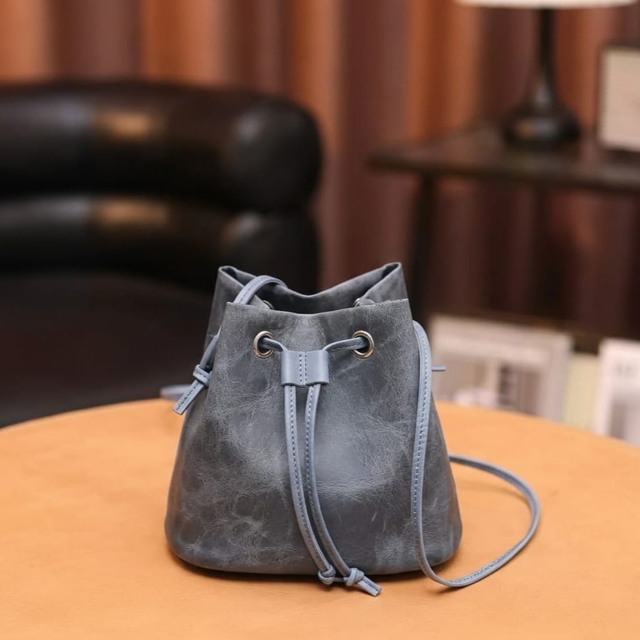 Gray suede drawstring bag on a wooden surface with a blurred background