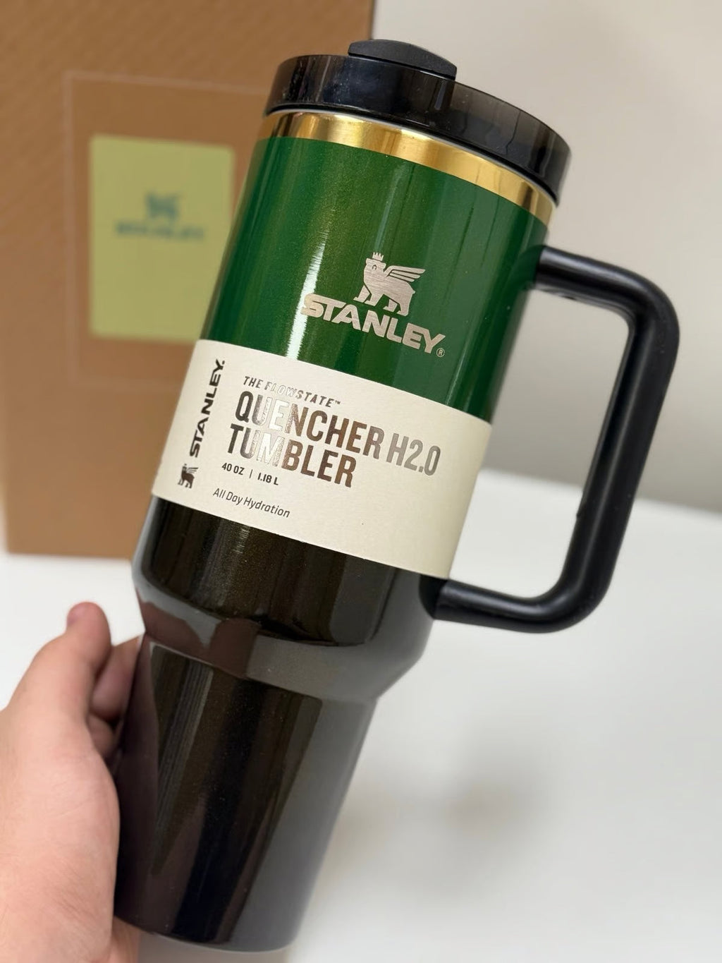 Green Stanley Quencher H2.0 tumbler held by a hand on a neutral background
