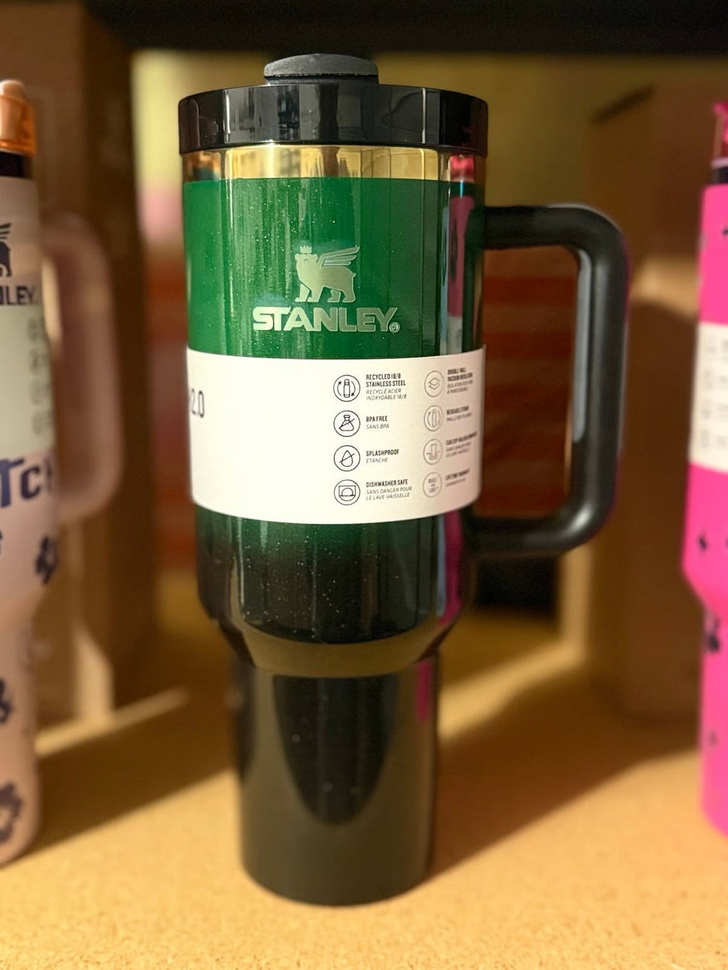 Green Stanley travel mug on a wooden surface with blurred background
