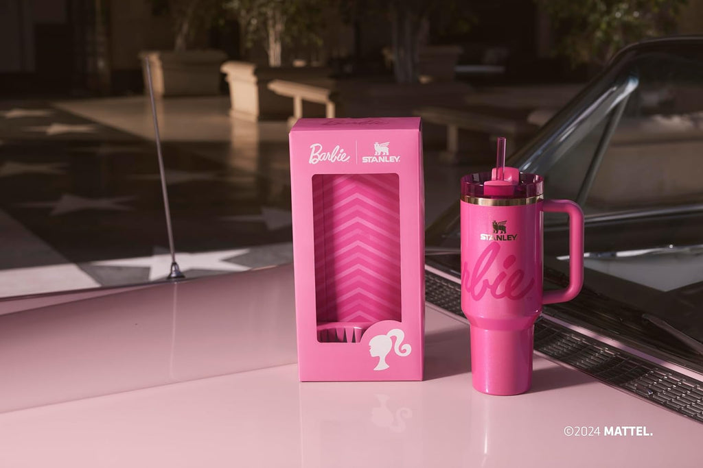 Pink 'Barbie' mug and packaging on a car hood with a pool and chairs in the background.