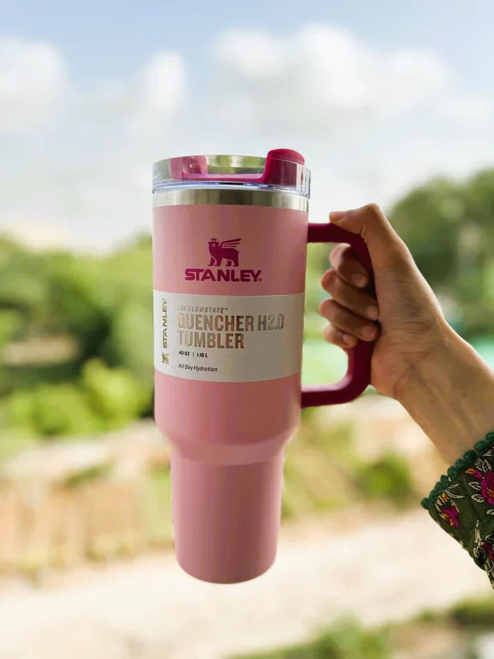 Pink Stanley tumbler held outdoors with a blurred natural background