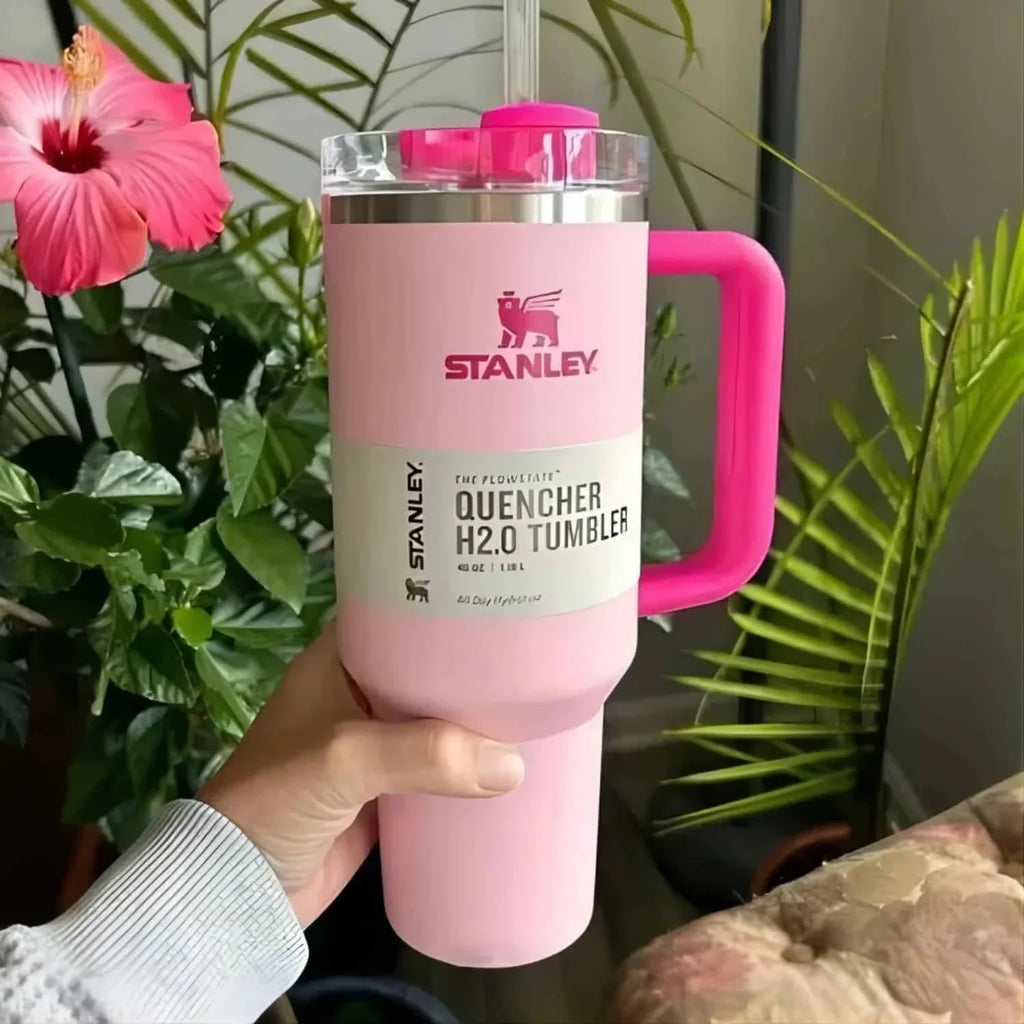 Pink Stanley tumbler with a handle held in front of plants