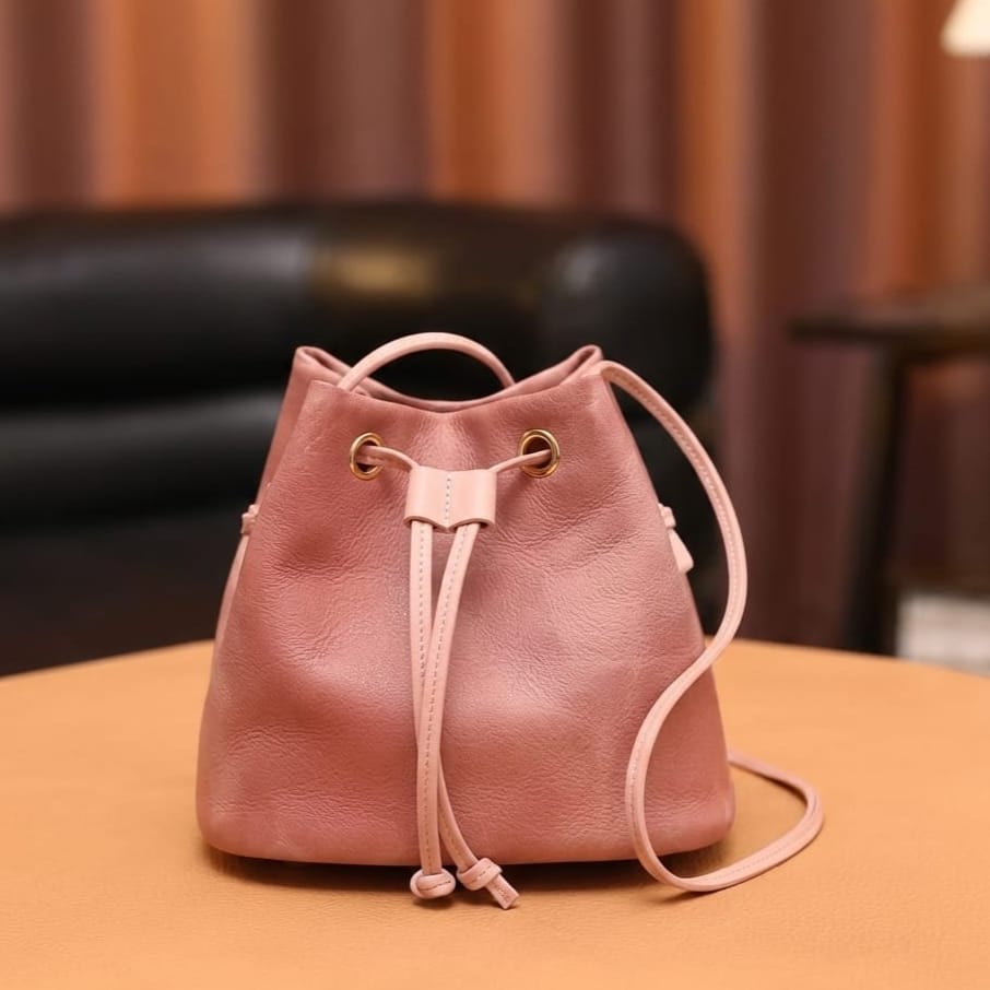 Pink leather drawstring bag on a wooden surface with a blurred background