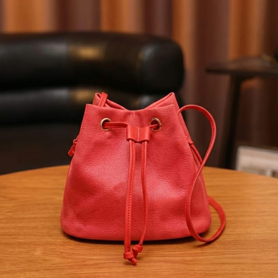 Red leather drawstring bag on a wooden table with a blurred background