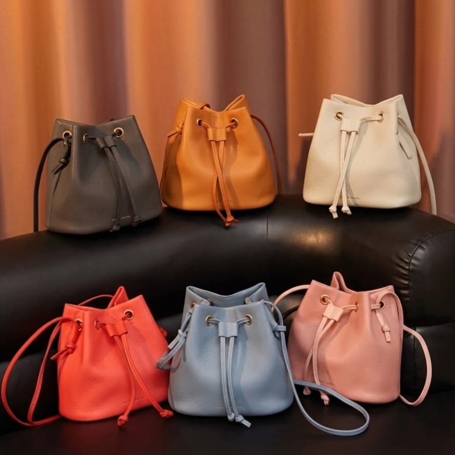 Six colorful drawstring bags on a black surface with a brown curtain background