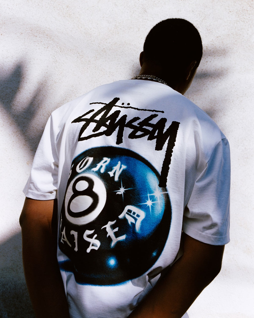 White Stussy x Born X Raised 8 Ball T-shirt from THE EA STORE, featuring a bold graphic design on the front.